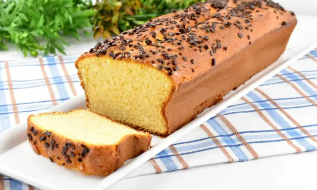 Puszysta babka z adwokatem, posypana czekoladową posypką, na białej paterze. Obok leży kromka ciasta.