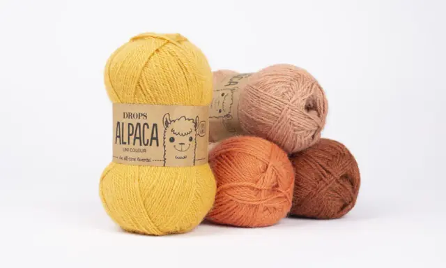 Garnnystan i varma färger som ockra, orange och rost. En guldig nystan från Drops Alpaca har en söt alpacka på etiketten.