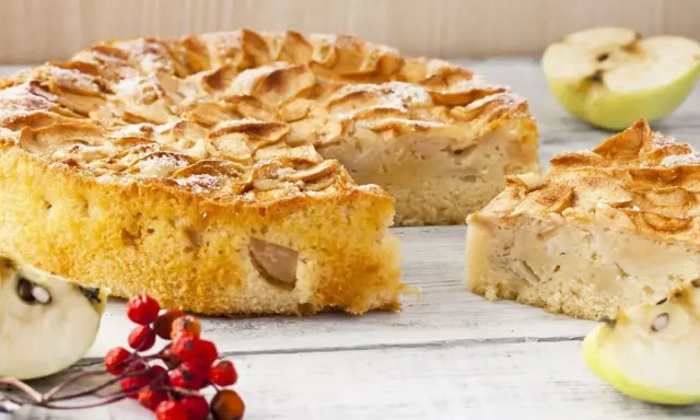 Un gâteau compote de pomme sans sucre, saupoudré de sucre glace, avec des quartiers de pomme et des baies rouges sur une table en bois.