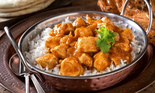 Un delicioso pollo al curry, un plato que evoca los sabores de la India, servido sobre arroz blanco en un cuenco de cobre.