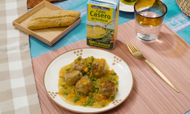 Albondigas a la jardinera en salsa con guisantes y zanahoria, acompañadas de pan y caldo de verduras.