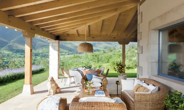 Ideas para como decorar porche de entrada: muebles de mimbre, mesa de comedor, un perro y vistas espectaculares.
