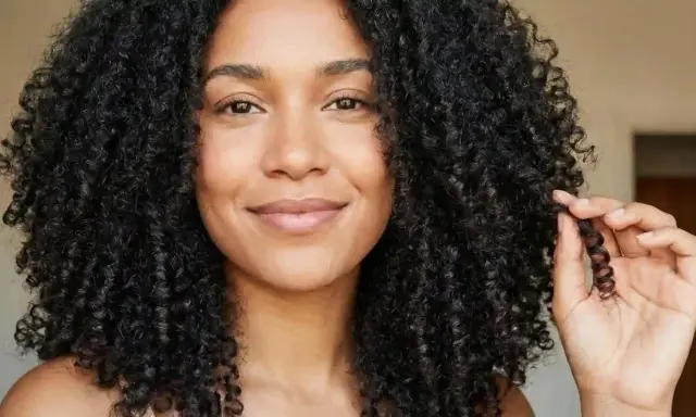 Une femme aux cheveux bouclés et brillants, elle joue avec une mèche formant un joli noeud boucle.