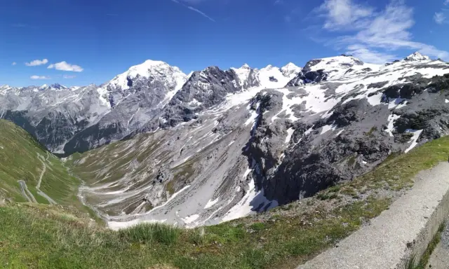 Panoramica mozzafiato dei fotografi sui tornanti dello Stelvio, con vette innevate e un cielo azzurro intenso.