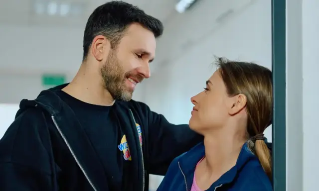 Uśmiechnięty mężczyzna patrzy na kobietę, która opiera się o ścianę. Może rozmawiają o tym, jak czytać mangę.
