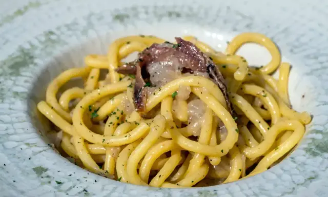 Un piatto di spaghetti con acciughe e prezzemolo, un'ottima idea per scoprire cosa mangiare a Padova.
