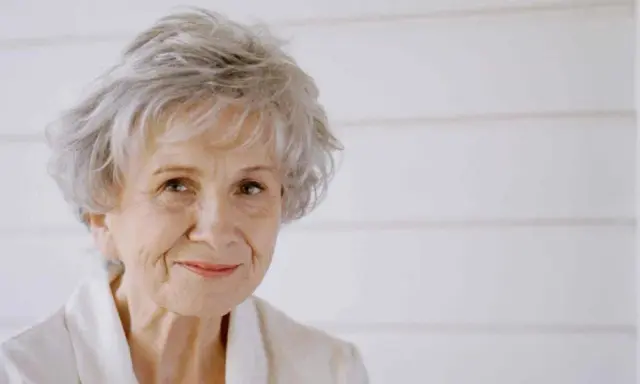 Ritratto di Alice Munro, con capelli grigi spettinati e un sorriso gentile.