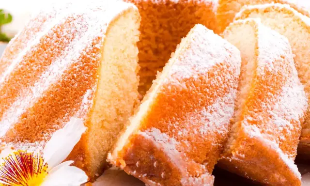 Szybka babka wilgotna, oprószona cukrem pudrem, z widocznymi kawałkami ciasta i ozdobiona kwiatem.