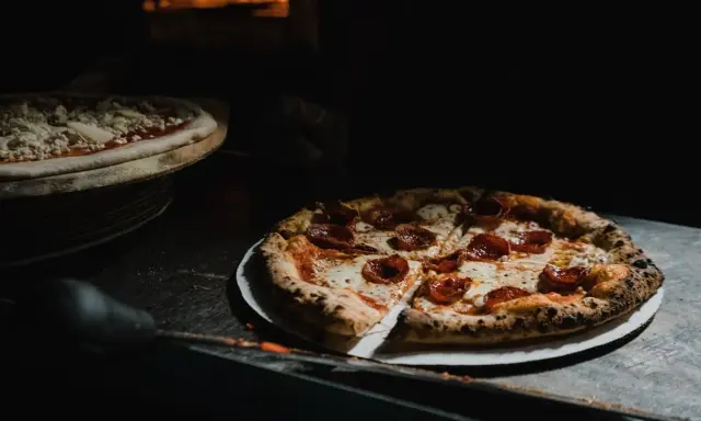 Upieczona pizza pepperoni na talerzu, obok surowa pizza w piecu.