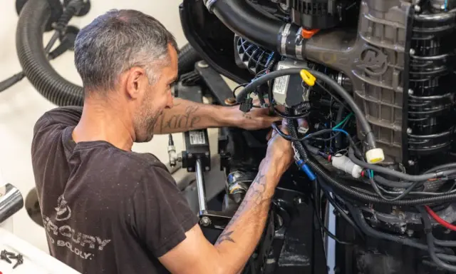 Un mécanicien s'affaire sur un moteur électrique, câbles et tuyaux visibles. Il sait comment tester un moteur électrique pour assurer son bon fonctionnement.