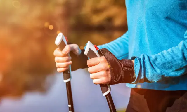 Radość z aktywnego życia po przeszczepie nerki. Dłonie trzymające kije do nordic walking na tle jesiennego krajobrazu.