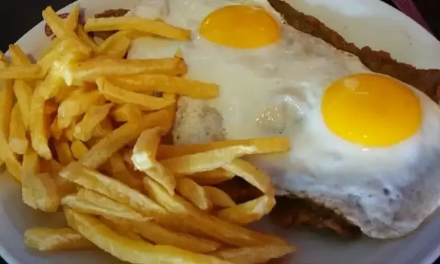 Un plato de milanesa a caballo argentina con papas fritas doradas y dos huevos fritos con yemas perfectas.