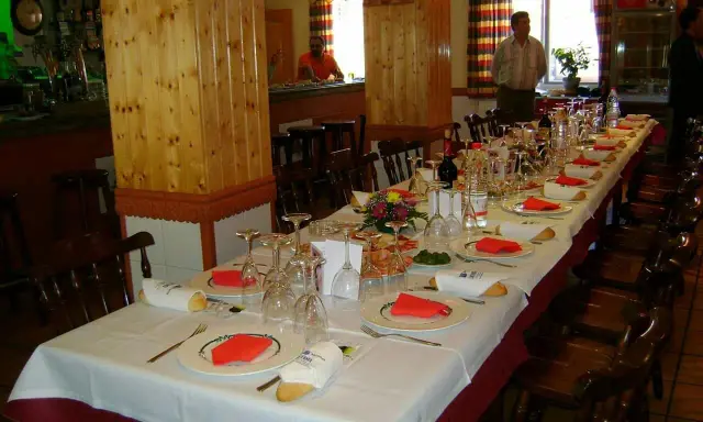 Mesa larga y elegante lista para comer en Riopar, con copas, platos y panecillos.