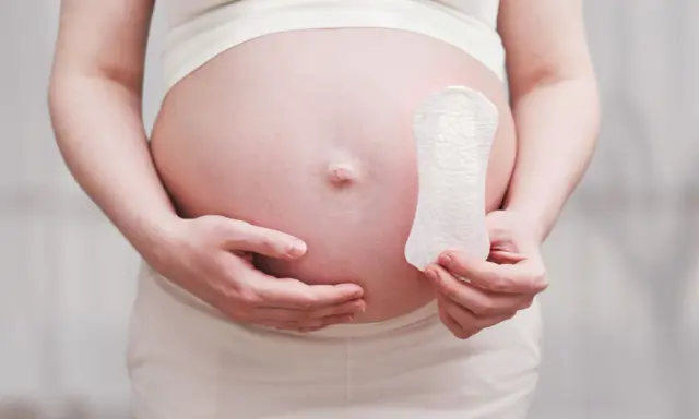 Ciężarna kobieta trzyma podpaskę, sugerując pytanie: czy w okres można zajść w ciążę?