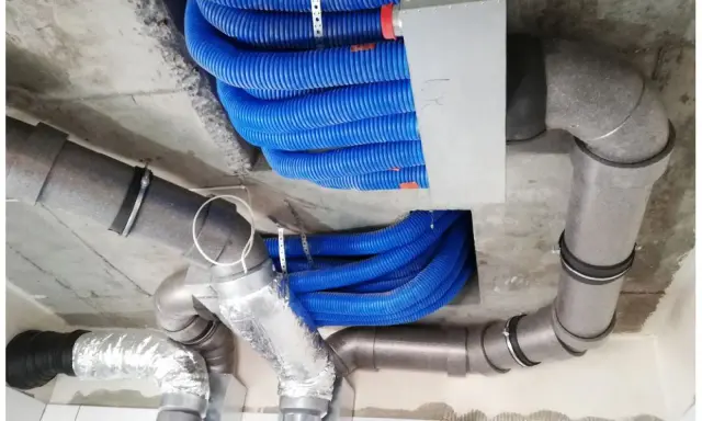 Instalacja rekuperacji w starym domu: niebieskie przewody wentylacyjne i szare rury izolowane, zamontowane pod sufitem.
