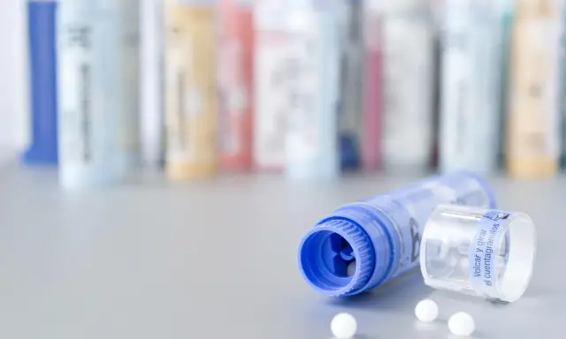 Flacons de granules homéopathiques, certains en arrière-plan floutés. Un tube bleu ouvert laisse échapper quelques billes blanches. Une solution naturelle pour la dermite séborrhéique, comme une huile essentielle, pourrait être contenue dans ces remèdes.