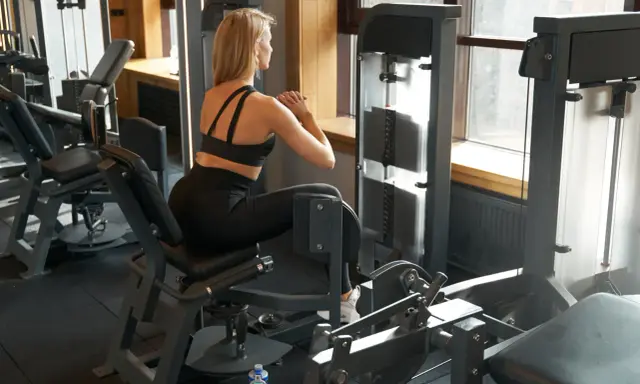 Frau trainiert im Fitnessstudio an einem Gerät für Bauch, Beine und Po.