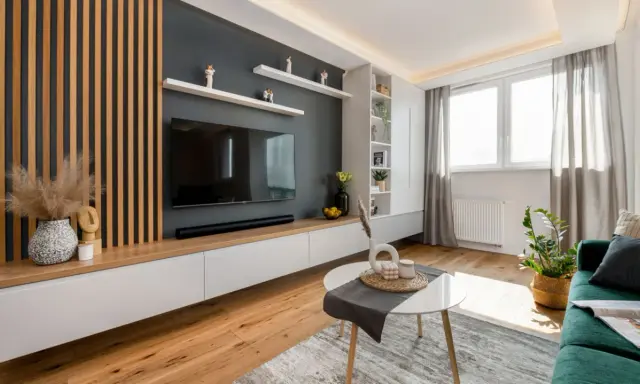 Nowoczesny salon z lamelami inspiracje: drewniane panele, szara ściana z TV, białe meble i zielona kanapa tworzą przytulną przestrzeń.