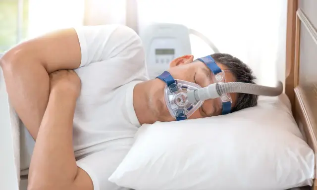 Mężczyzna śpi z maską CPAP, która pomaga mu oddychać podczas snu, łagodząc objawy bezdechu nocnego.