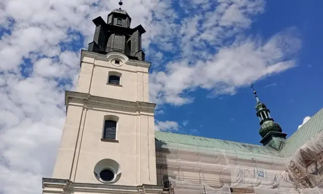 Wieża kościoła w Gidlach pod błękitnym niebem z chmurami. Widać fragment dachu w rusztowaniach.