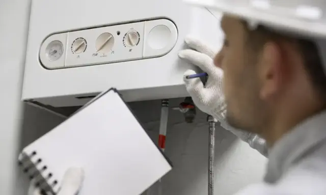 Técnico revisa una caldera de condensación, anotando detalles en su libreta.