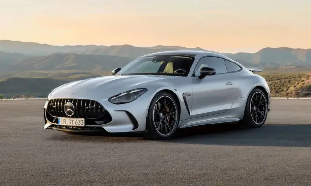 Un elegante Mercedes GTR plateado descansa en una carretera desierta, con montañas onduladas al atardecer de fondo.