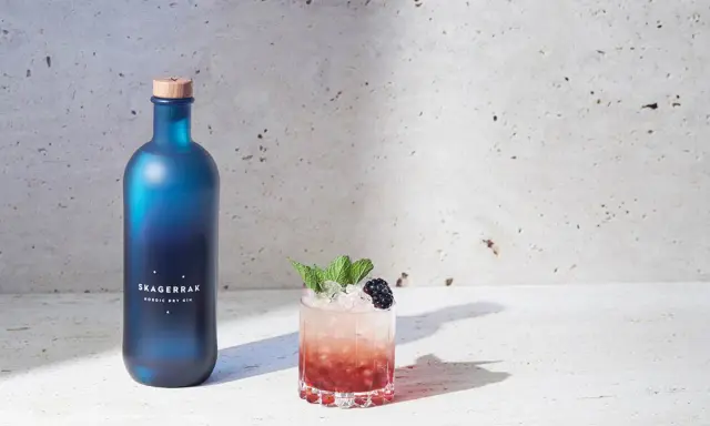 En blå flaska Skagerrak Nordic Dry Gin bredvid en läcker bramble drink med björnbär och mynta.