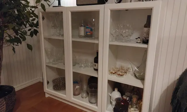 Ett DIY-projekt med ett vitt Billy vitrinskåp fyllt med glas, flaskor och dekorationer.