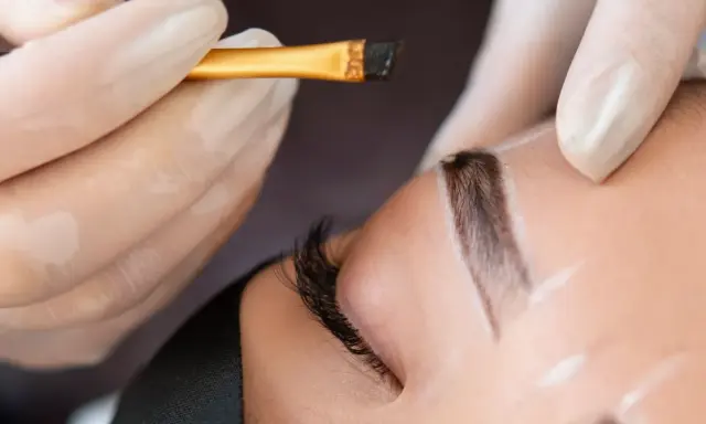 Application d'une teinture sourcils en institut. Un pinceau fin dépose la couleur sur un sourcil soigneusement dessiné.