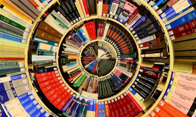 Książki ułożone w spiralę, tworząc piotr kościelny dom wiedzy. Widać tytuły o naukach ścisłych i przyrodniczych.