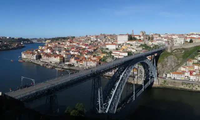 El icónico puente de Oporto cruza el río Duero, conectando la ciudad con sus coloridas casas y barcos turísticos.