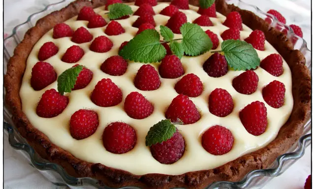 Tarta z mascarpone i białą czekoladą, ozdobiona malinami i miętą. Pyszny deser na każdą okazję.