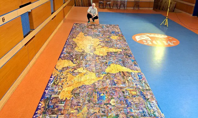 Mężczyzna kuca przy największych puzzlach na świecie, przedstawiających mapę świata z detalami miast.