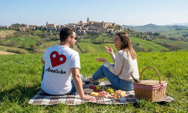 Coppia in un prato verde con vista su un borgo collinare. Perfetto per scoprire cosa fare a Pasquetta nelle Marche con un picnic.