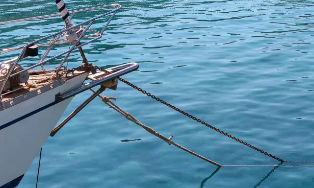 L'étrave d'un voilier blanc est ancrée dans une eau bleue et claire. La chaîne et la corde sont bien visibles, prêtes à mouiller beaucoup.
