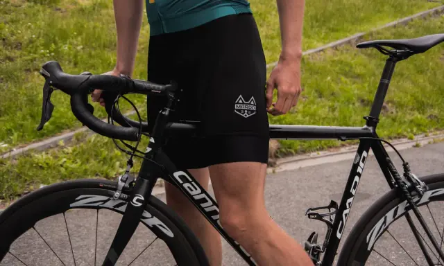 Kolarz w czarnych spodenkach i zielonej koszulce przygotowuje się do treningu kolarskiego. Rower szosowy Cannondale czeka na jazdę.