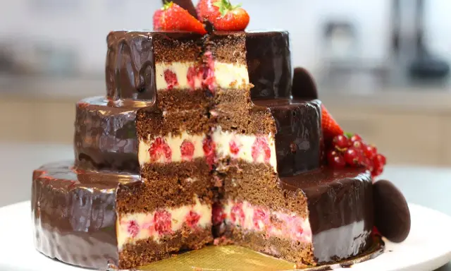 Gâteau à trois étages au chocolat et aux framboises, parfait pour une recette gâteau anniversaire facile. Décoré de fruits rouges et de chocolat.
