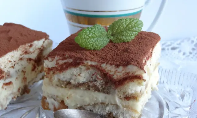 Pyszne tiramisu bezglutenowe, posypane kakao i udekorowane listkiem mięty, czeka na łyżeczkę.