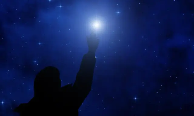 Sylwetka człowieka sięga ku jasnej gwieździe polarnej na tle nocnego, gwiaździstego nieba.