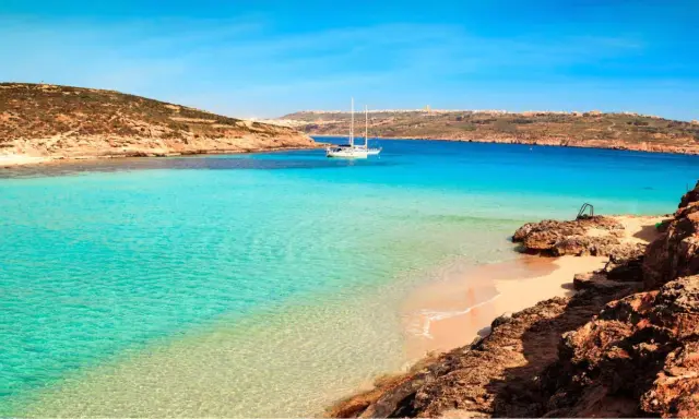 Traumhafter Malta Strand mit türkisfarbenem Wasser, einer einsamen Bucht und einem Segelboot. Perfekt für einen entspannten Urlaub.