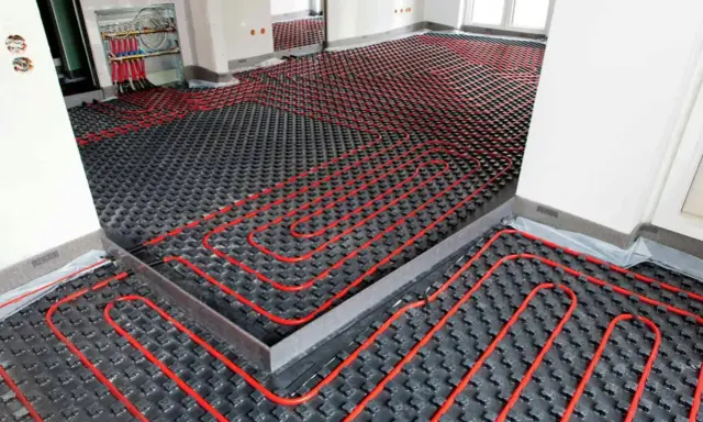 Instalación de suelo radiante con tuberías rojas sobre paneles negros, preparado para aerotermia.