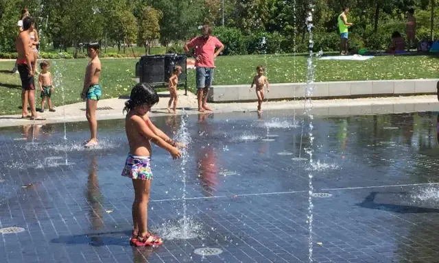 Niños y adultos disfrutan del agua en las fuentes del madrid rio parque.