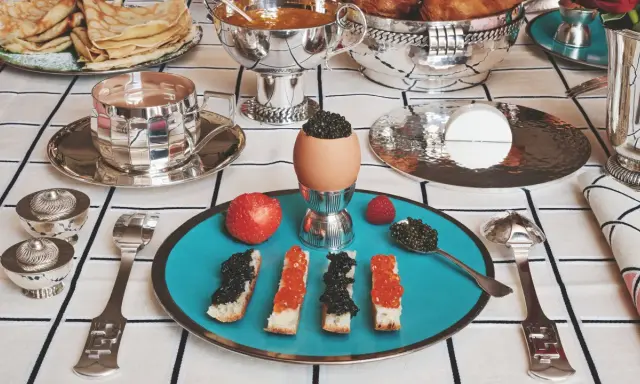 Un service de table à la française élégant pour un petit-déjeuner luxueux : toasts au caviar, œufs, fruits et crêpes.