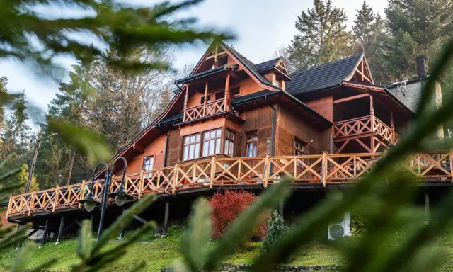 Drewniane schronisko turystyczne z tarasem i balustradą, otoczone drzewami.