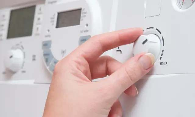 Mano ajustando el dial de una caldera de gas para cambiar la temperatura.