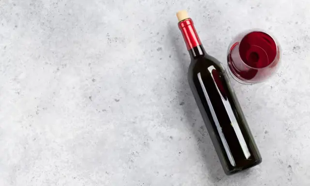 En flaska tamaral vin och ett glas rött vin på ett grått, stenig bakgrund.