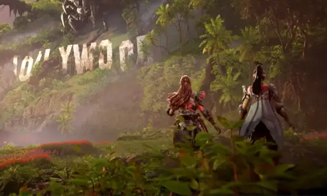 Aloy i jej towarzyszka przemierzają bujną dżunglę w Horizon Forbidden West: Burning Shores, mijając zniszczony napis Hollywood.