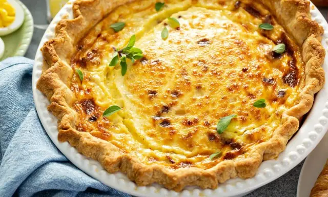 Une délicieuse quiche lorraine, un classique des plats lorrains, garnie de feuilles vertes.