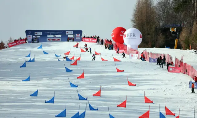 Zawodnicy snowboardu pokonują trasę z czerwonymi i niebieskimi tyczkami na stoku Jaworzyny Krynickiej.