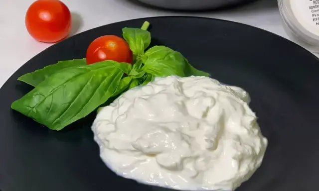 En krämig hög av stracciatella ost med färska basilikablad och körsbärstomater på en svart tallrik.